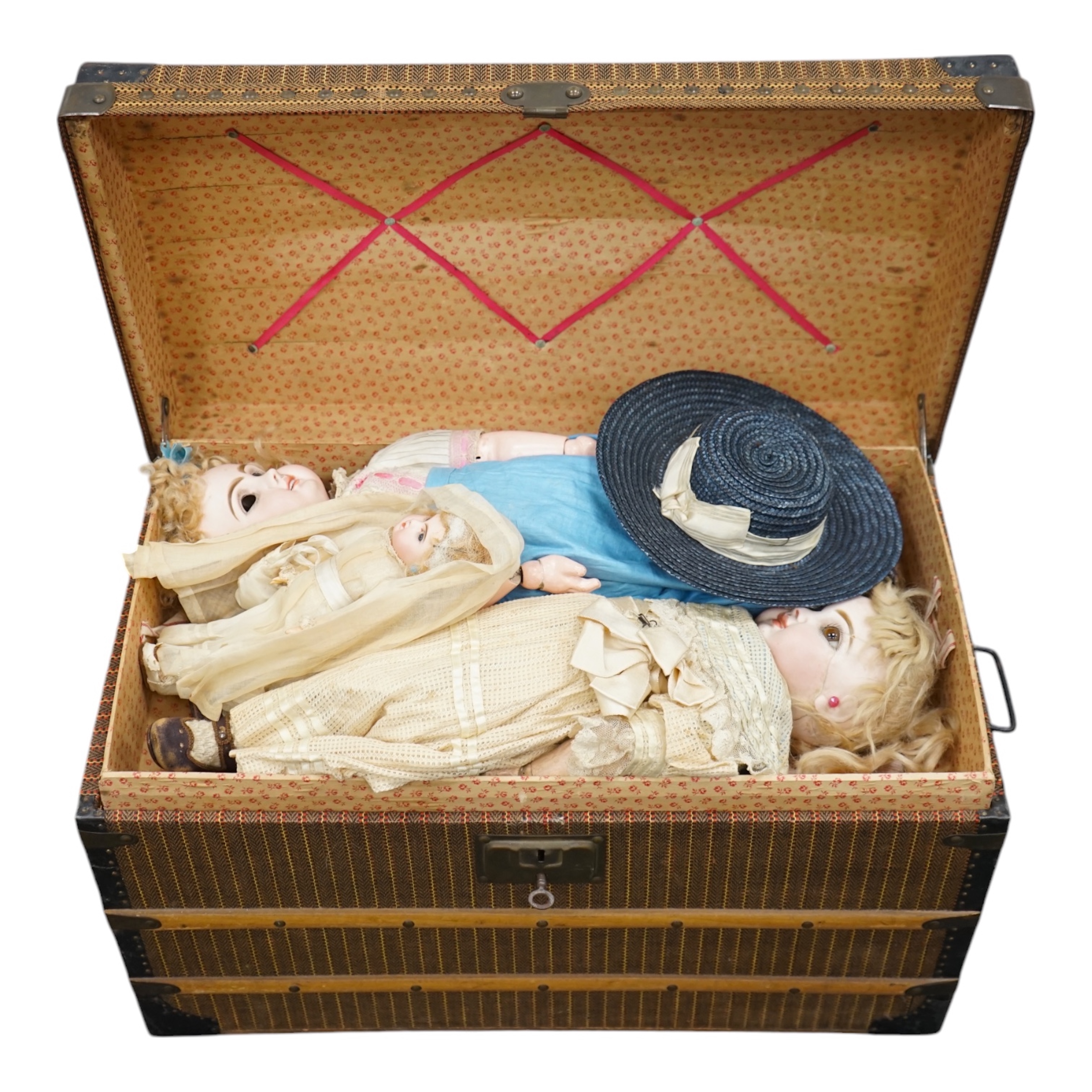 A Tête Jumeau bisque doll, closed mouth and paperweight eyes, jointed wood and composition body, two other French bisque dolls and assorted clothing, all contained within a three-layer wood and metal-bound cabin trunk, J